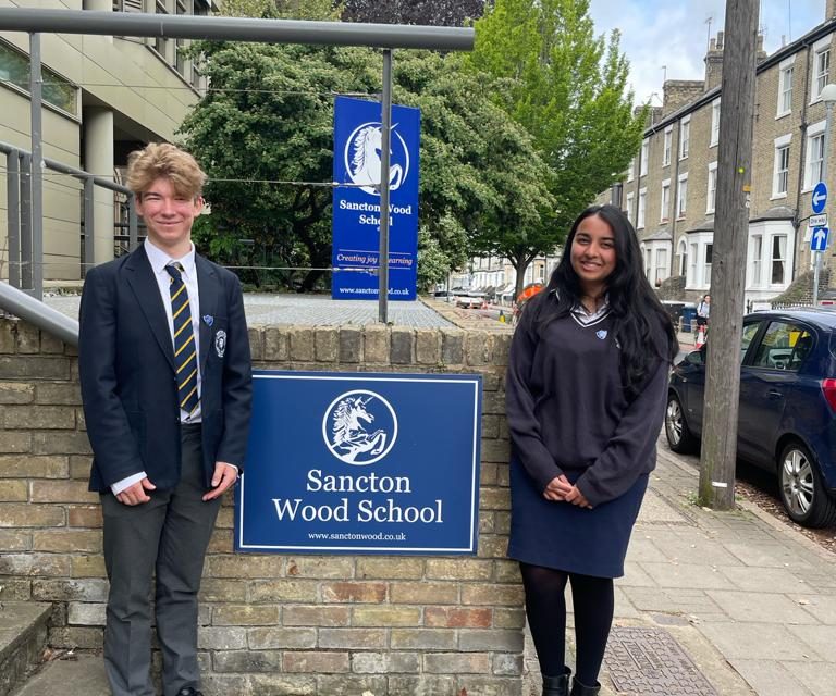two students standing infront of a sancton wood school poster