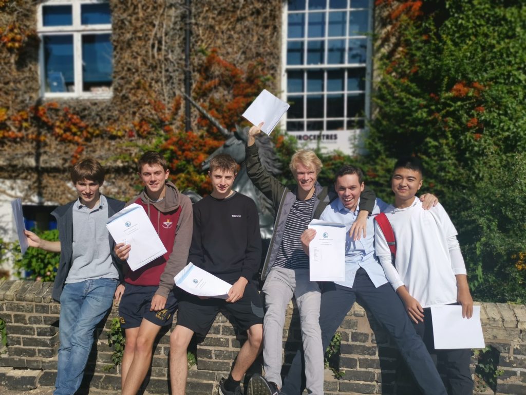 students sat on a brick wall celebrating their GCSE results
