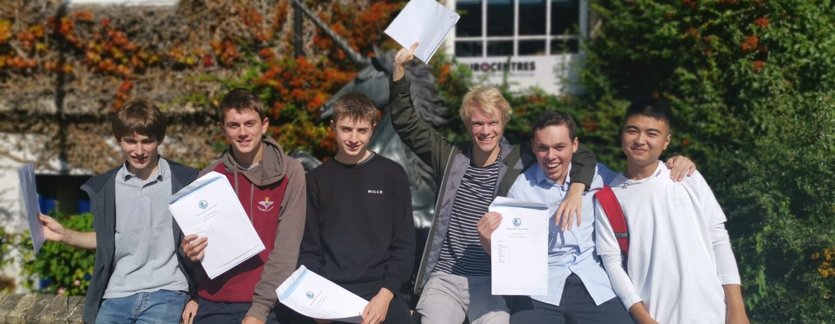 students sat on a brick wall celebrating their GCSE results