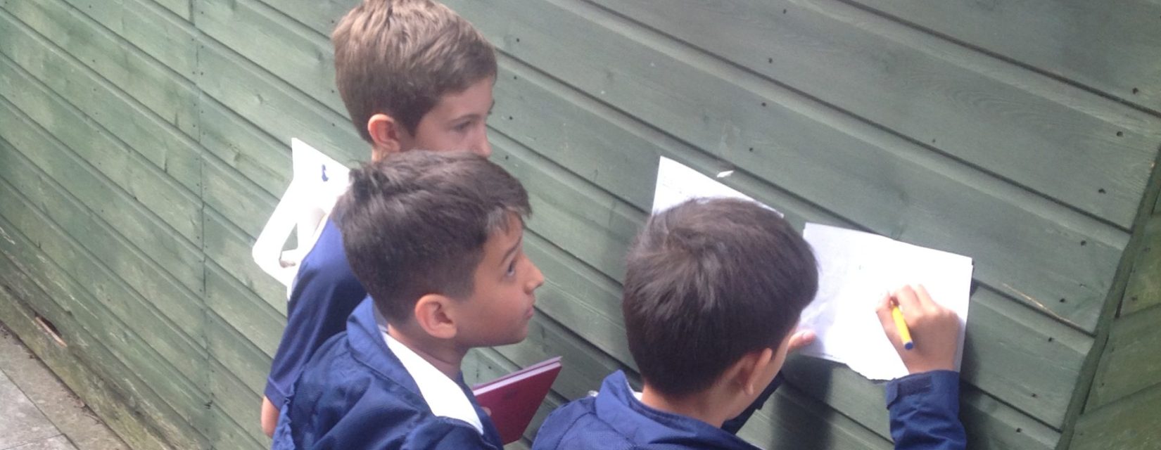 children leaning against a shed to write